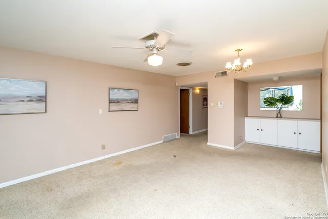 an empty room with a chandelier fan and windows