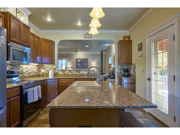 a kitchen with granite countertop a stove a sink a refrigerator and blue cabinets with wooden floor