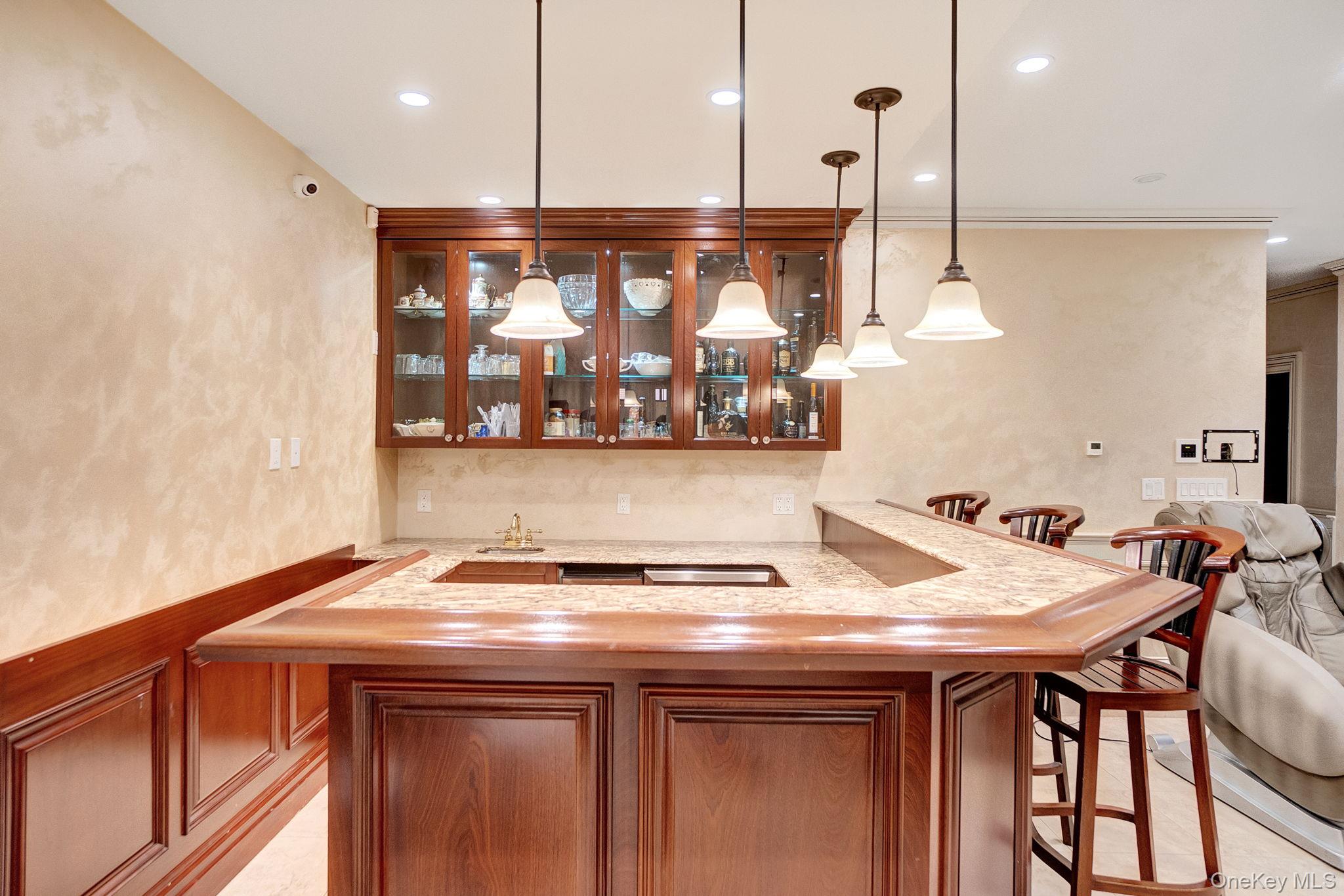 181-30 Tudor Road Queens, NY 11432 - Photo 38 of 46 Indoor wet bar featuring glass insert cabinets, pendant lighting, light stone counters, recessed lighting, and brown cabinets