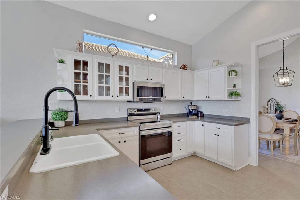 15464 Cortona Way Naples, FL 34120 - Photo 15 of 47 Kitchen with open shelves, stainless steel appliances, white cabinets, lofted ceiling, and glass insert cabinets