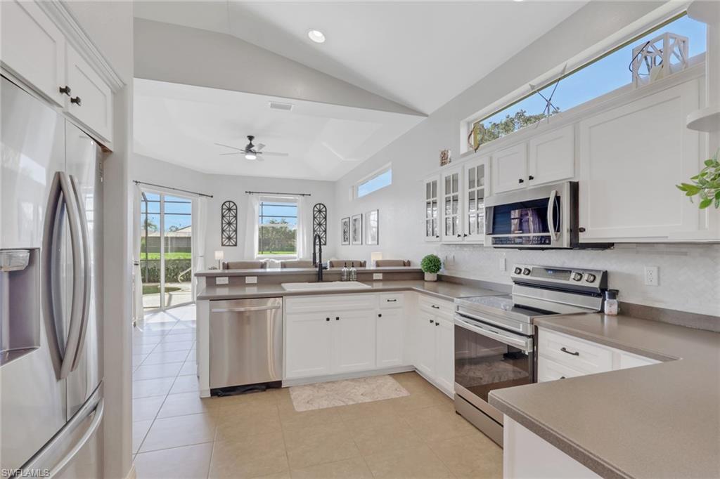 15464 Cortona Way Naples, FL 34120 - Photo 16 of 47 Kitchen featuring appliances with stainless steel finishes, a peninsula, white cabinetry, vaulted ceiling, and glass insert cabinets