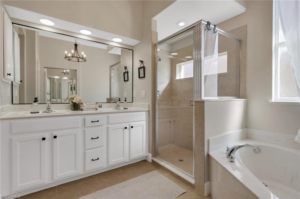 15464 Cortona Way Naples, FL 34120 - Photo 20 of 47 Bathroom with double vanity, a shower stall, a garden tub, light tile patterned flooring, and a chandelier