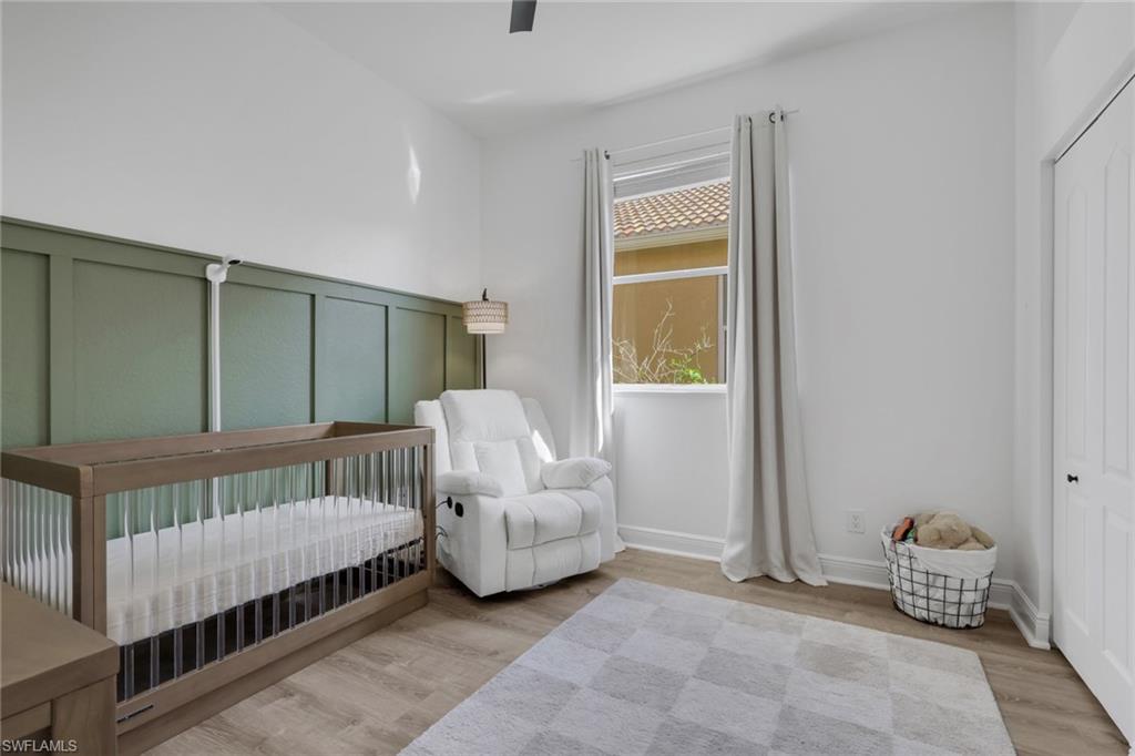 15464 Cortona Way Naples, FL 34120 - Photo 25 of 47 Bedroom featuring a nursery area, light wood-style flooring, ceiling fan, and a decorative wall