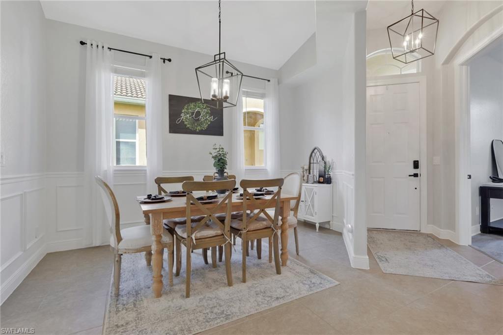 15464 Cortona Way Naples, FL 34120 - Photo 5 of 47 Dining space featuring a chandelier, vaulted ceiling, healthy amount of natural light, wainscoting, and a decorative wall