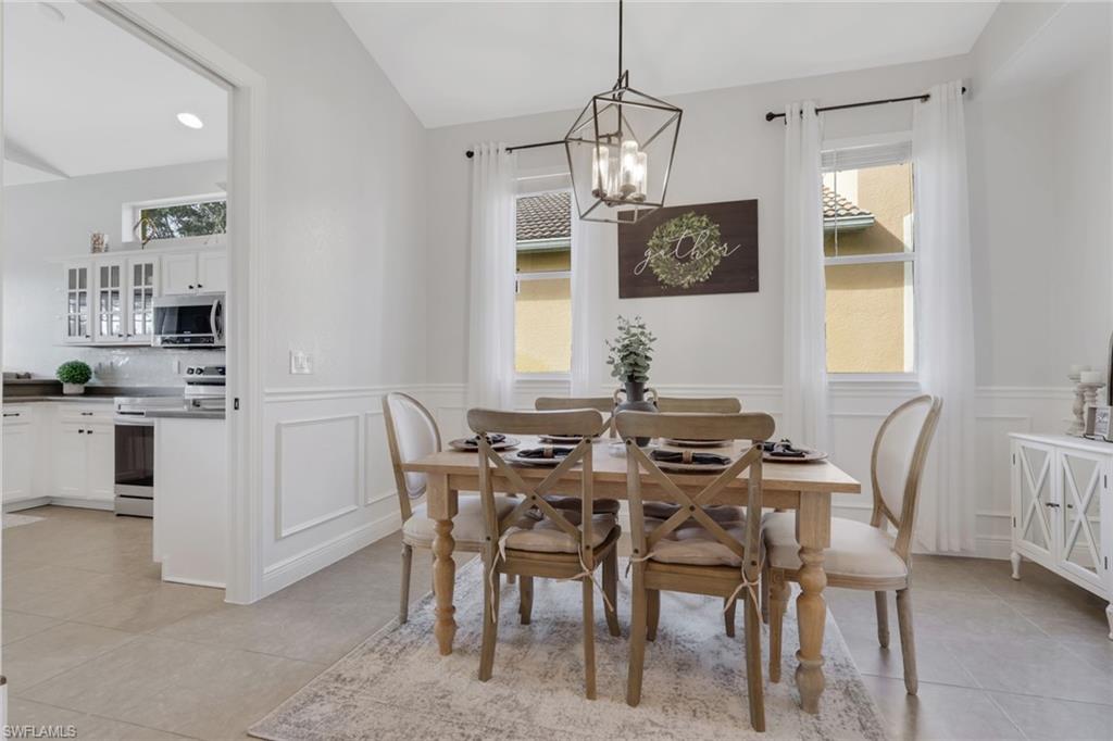 15464 Cortona Way Naples, FL 34120 - Photo 6 of 47 Dining space with light tile patterned floors, a chandelier, wainscoting, and lofted ceiling
