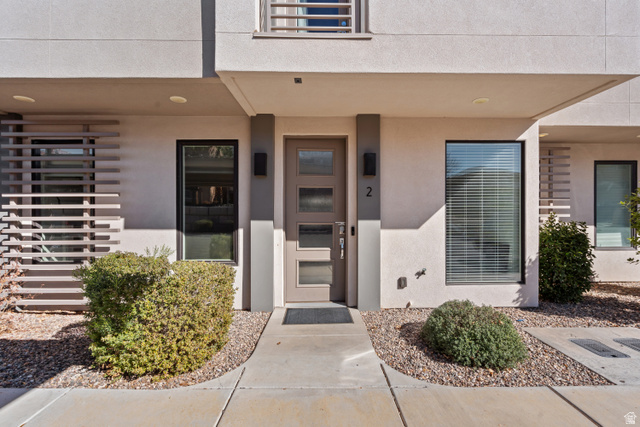 1122 South 1790th Street West, Unit 2 St. George, UT 84770 - Photo 2 of 37 Contemporary stucco exterior featuring a modern entry door with frosted glass panels, black-framed windows, decorative horizontal slat detailing, and low-maintenance gravel landscaping
