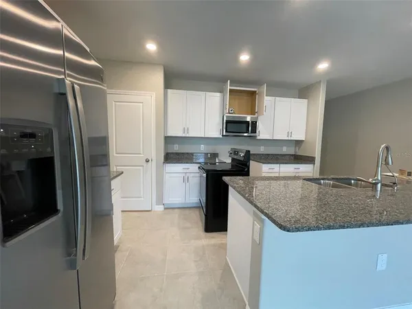 a kitchen with kitchen island granite countertop a refrigerator a sink a stove a microwave and island