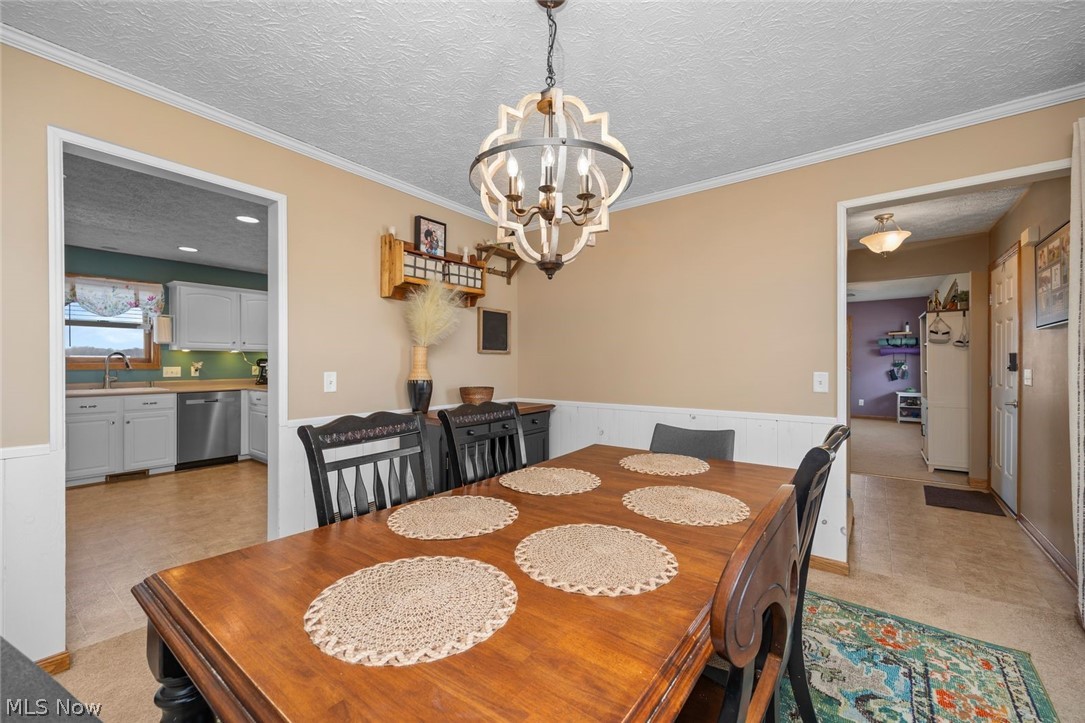 4273 Old State Road Willard, OH 44890 - Photo 11 of 50 Dining space featuring a textured ceiling, a wainscoted wall, suspended lighting, light floors, and ornamental molding