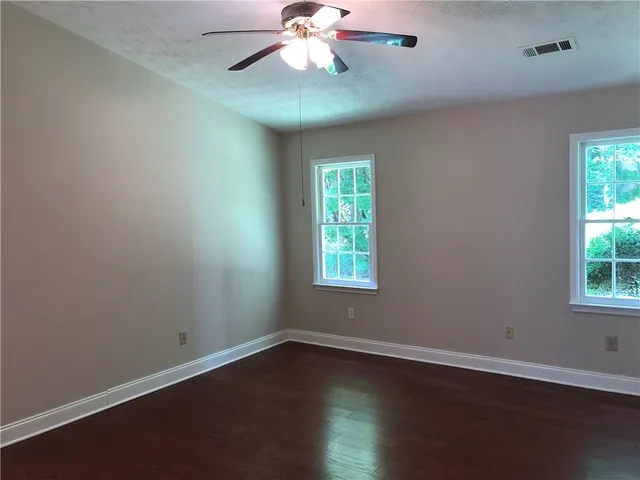 an empty room with wooden floor chandelier fan and windows