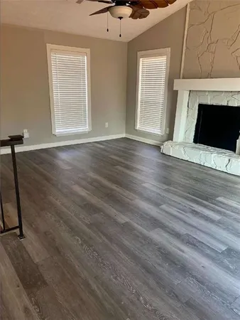 an empty room with wooden floor fireplace and windows