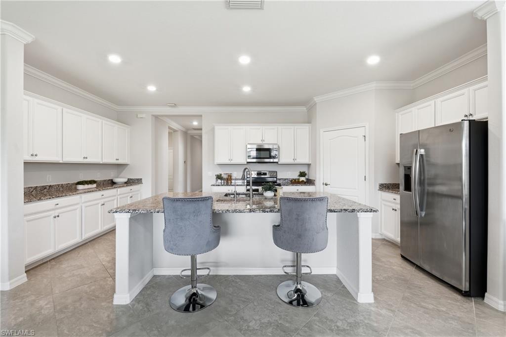 4374 Bismark Way Naples, FL 34119 - Photo 9 of 49 Kitchen featuring an island with stone countertops, stainless steel appliances, white cabinetry, recessed lighting, and tile flooring