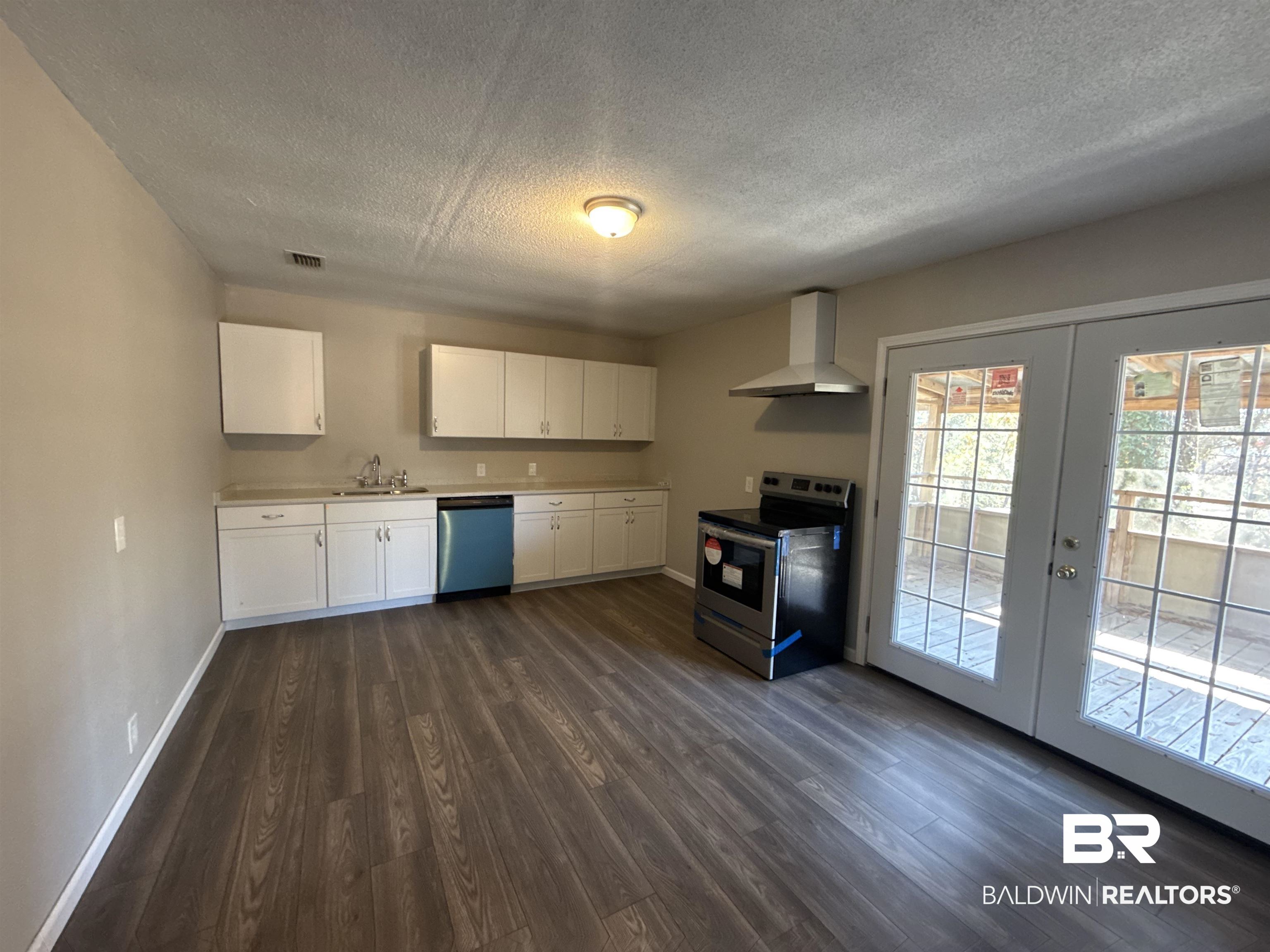 32 Slate Street Atmore, AL 36502 - Photo 6 of 16 Kitchen featuring appliances with stainless steel finishes, white cabinets, light countertops, a textured ceiling, and wall chimney exhaust hood