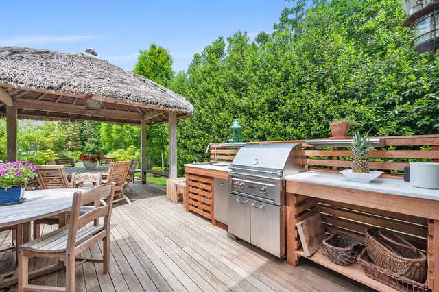 a view of a patio with table and chairs under an umbrella with a barbeque