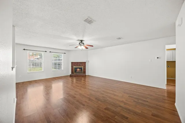 an empty room with wooden floor chandelier fan and windows