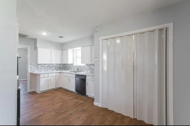 a large white kitchen with a refrigerator a sink dishwasher and white cabinets with wooden floor