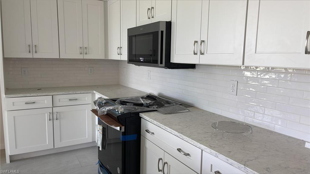 14557 Kingfisher Loop Naples, FL 34120 - Photo 4 of 27 a kitchen with granite countertop white cabinets and black appliances