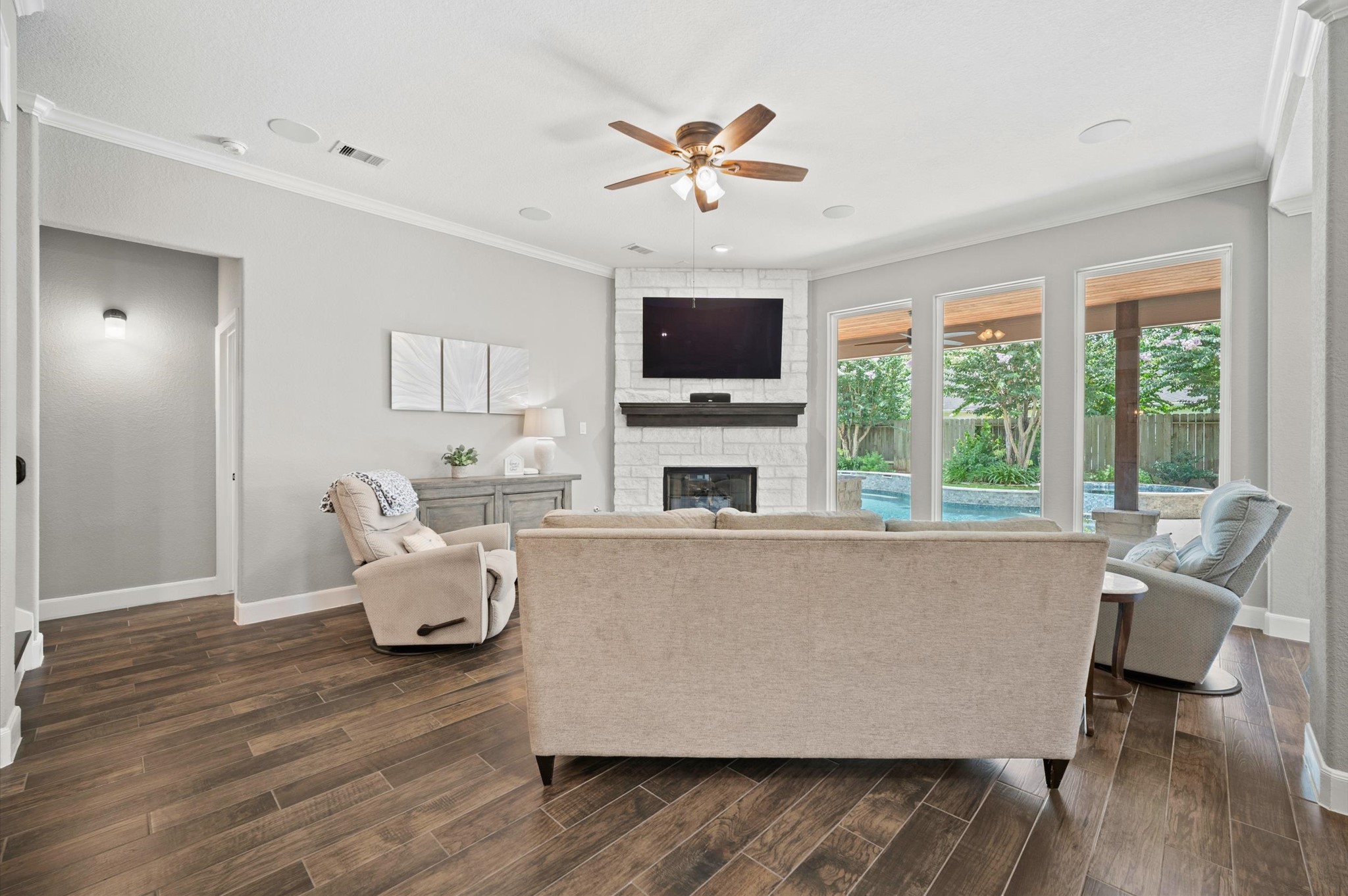 9507 Empress Crossing Drive Spring, TX 77379 - Photo 20 of 50 This inviting living room features a cozy stone fireplace, hardwood floors, and ample natural light from large windows overlooking a lush backyard with a pool. A ceiling fan adds comfort, while neutral tones provide a warm, modern feel.