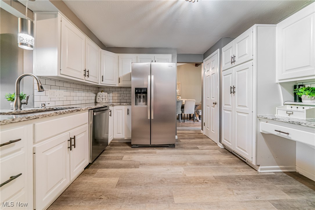 595 Moorfield Road Fairlawn, OH 44313 - Photo 8 of 50 Kitchen featuring appliances with stainless steel finishes, backsplash, white cabinets, light stone countertops, and light wood-style flooring