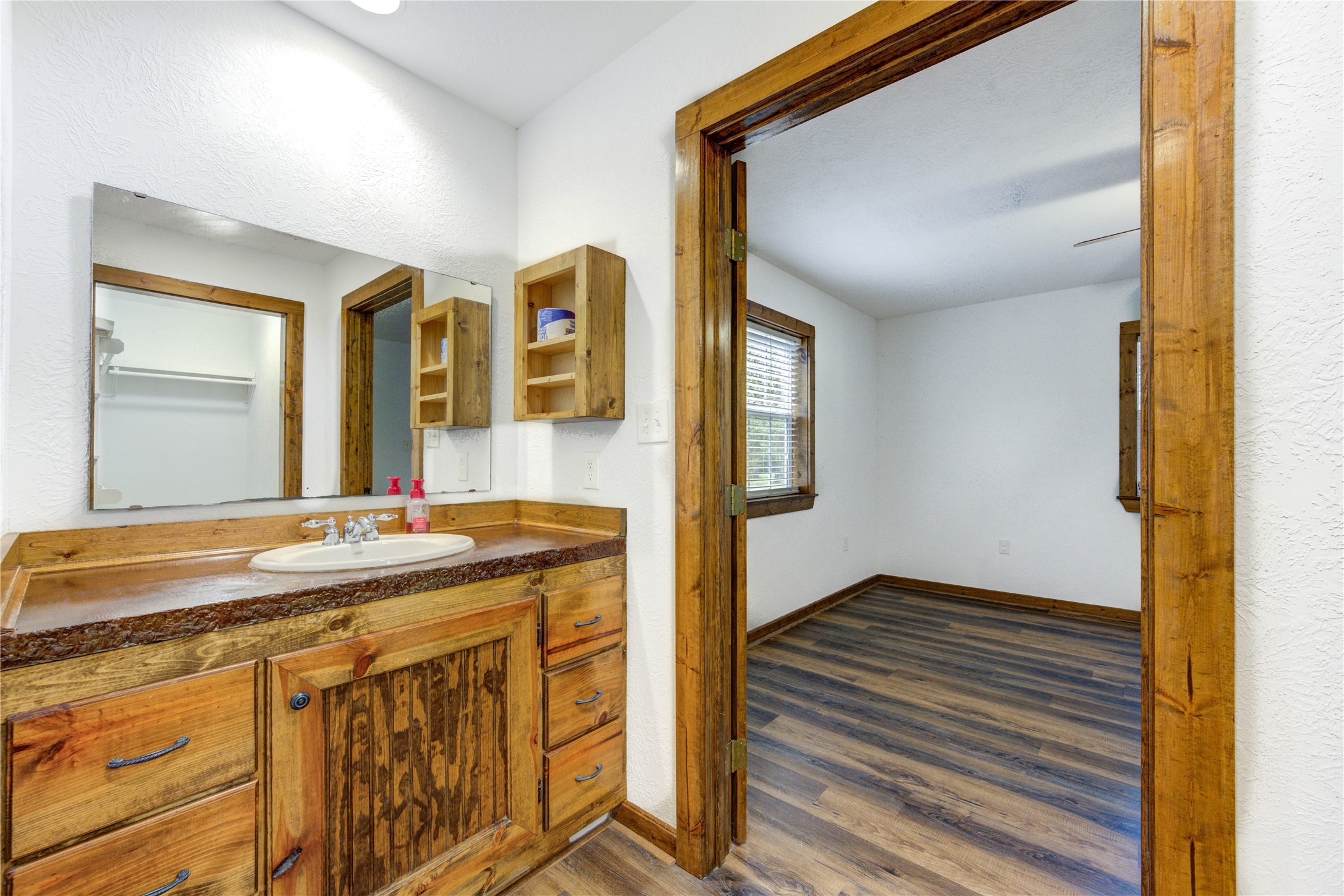 8805 Sun Oil Road Brenham, TX 77833 - Photo 28 of 50 Charming rustic bathroom featuring a wood-paneled vanity and ample storage, seamlessly connecting to a bright room with rich wood flooring.