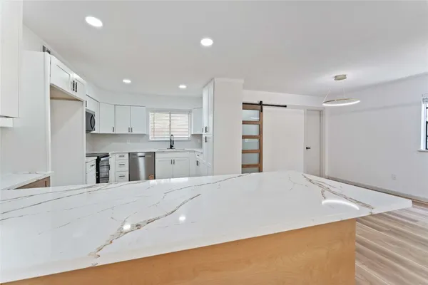 a large white kitchen with kitchen island a sink stainless steel appliances and cabinets