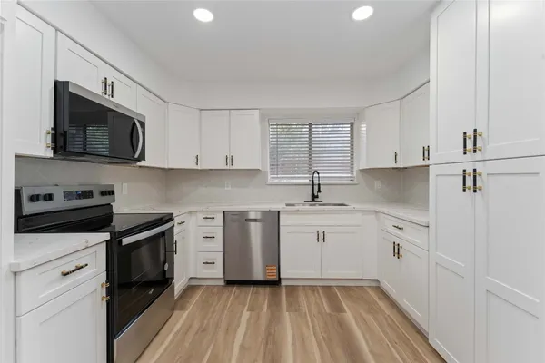 a kitchen with white cabinets appliances a sink and a window