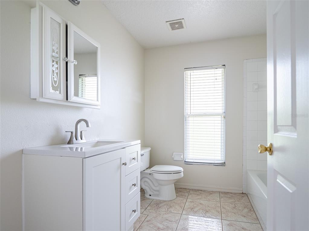 6569 Long Breeze Road Orlando, FL 32810 - Photo 23 of 31 a bathroom with a toilet a sink a mirror a window and vanity