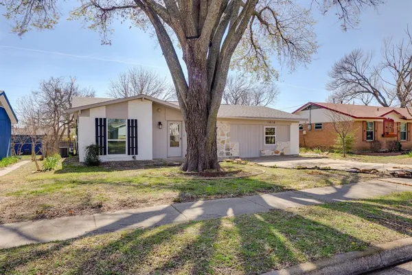 a view of a white house next to a yard with big trees and wooden fence