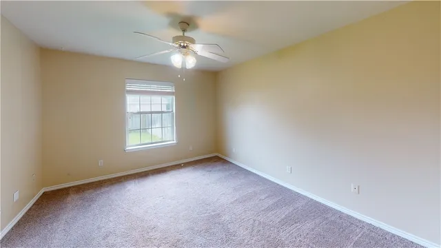 an empty room with a chandelier fan and windows