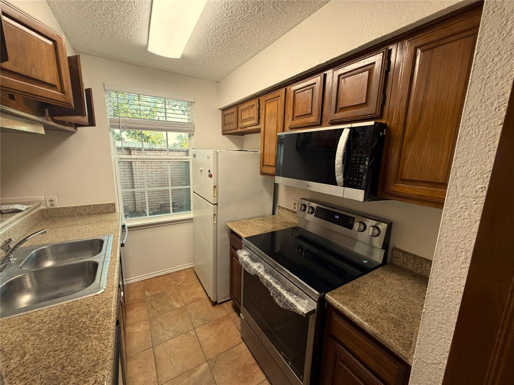 18240 Midway Road, Unit 206 Dallas, TX 75287 - Photo 6 of 16 Kitchen featuring warm wood cabinetry, neutral countertops, a double basin stainless steel sink, a stainless steel electric range, and an over-the-range microwave