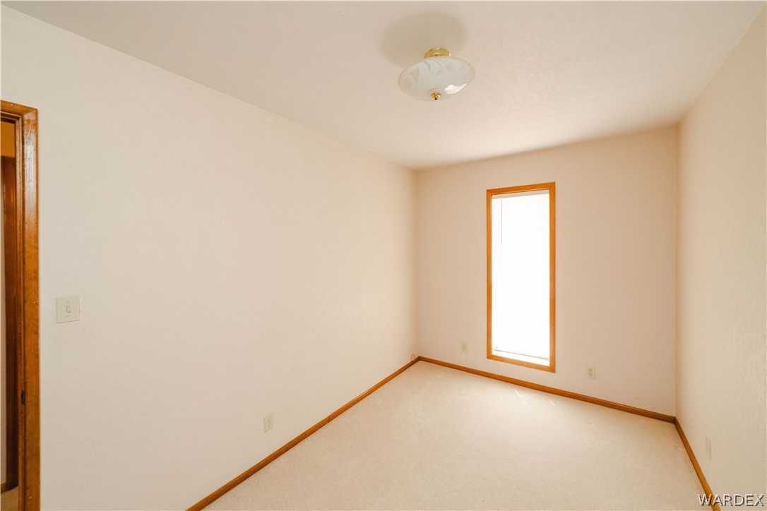 2100 East Valley View Road Kingman, AZ 86409 - Photo 27 of 53 Neutral-toned room featuring a single window with wood-finish trim, a flush-mount ceiling light fixture, and light-colored carpet flooring