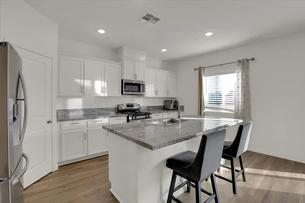 a kitchen with kitchen island granite countertop a sink stove refrigerator and white cabinets with wooden floor