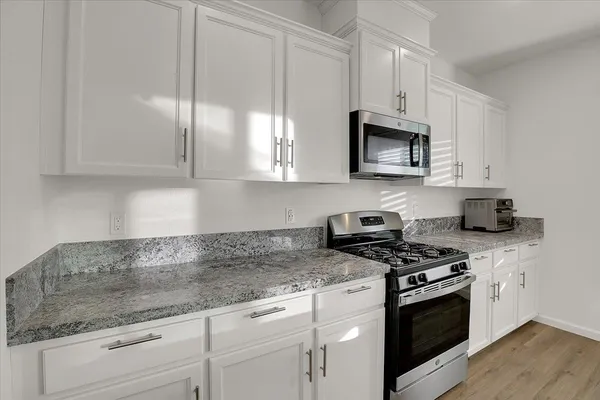 a kitchen with granite countertop white cabinets stainless steel appliances and a counter space