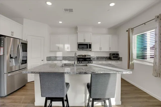 a kitchen with stainless steel appliances granite countertop a stove a sink a microwave a refrigerator and white cabinets