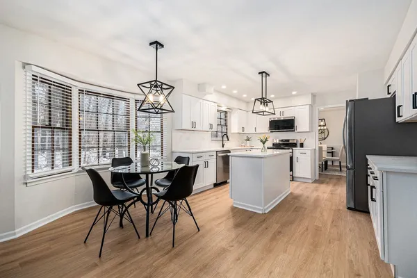 a kitchen with stainless steel appliances granite countertop a stove top oven a refrigerator a dining table and chairs with wooden floor