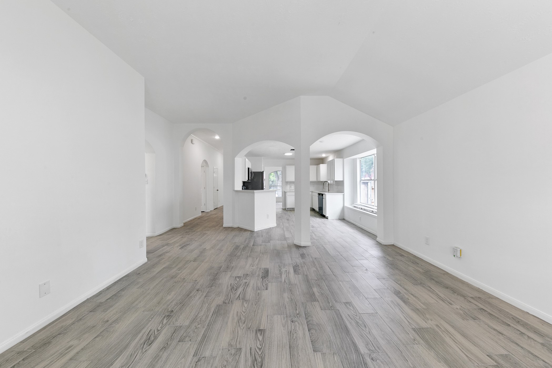 12014 Raven View Drive Houston, TX 77067 - Photo 16 of 29 This photo showcases a spacious, open-concept living area with light wood flooring and white walls. It leads into a bright kitchen with large windows and modern cabinetry, providing plenty of natural light.
