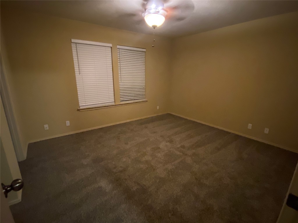 4527 Secure Lane, Unit 32 Austin, TX 78725 - Photo 7 of 9 Empty room with dark carpet and ceiling fan