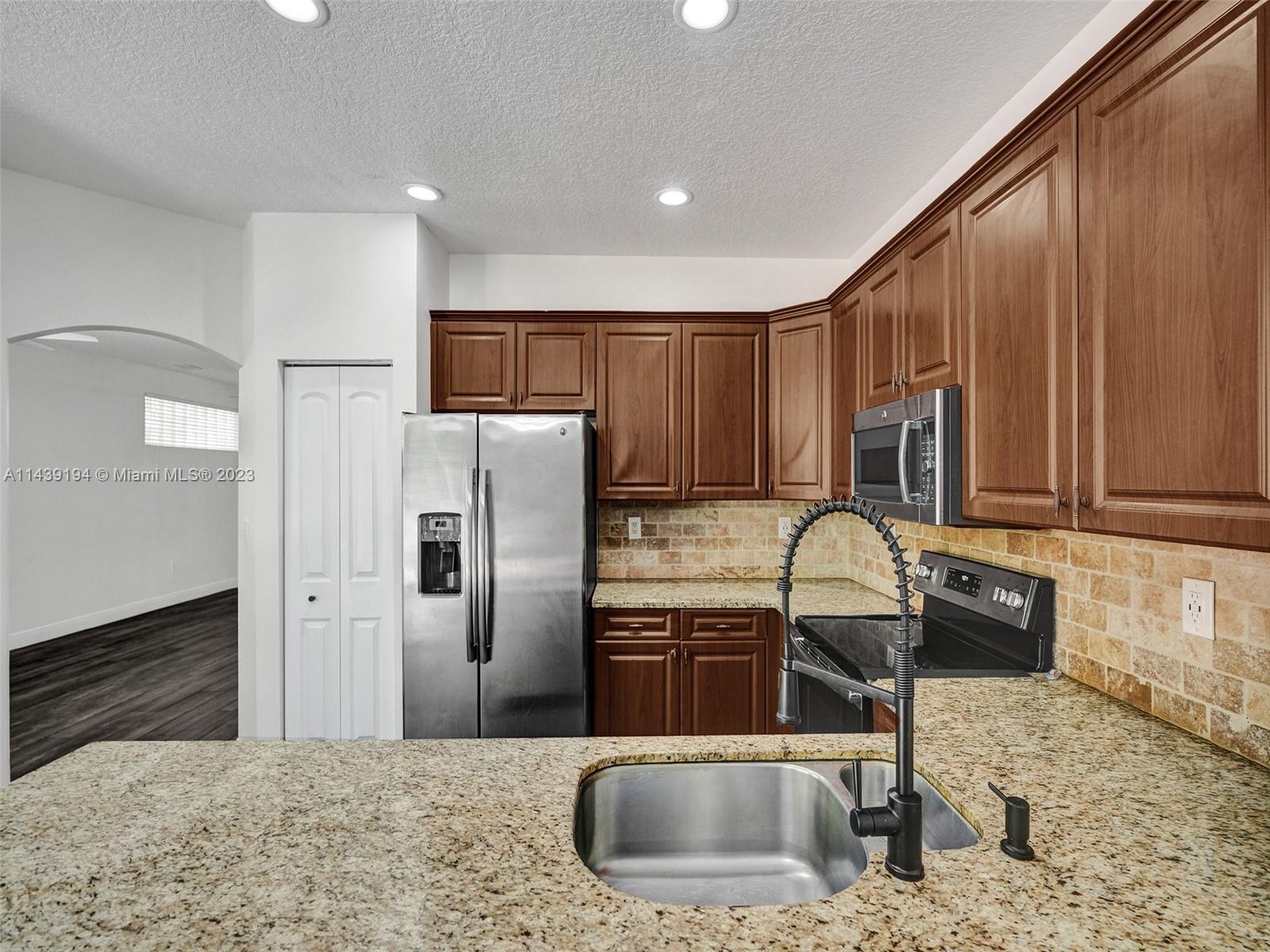4185 Tree Top Road Cooper City, FL 33026 - Photo 11 of 36 a kitchen with granite countertop a sink a refrigerator and a stove top oven