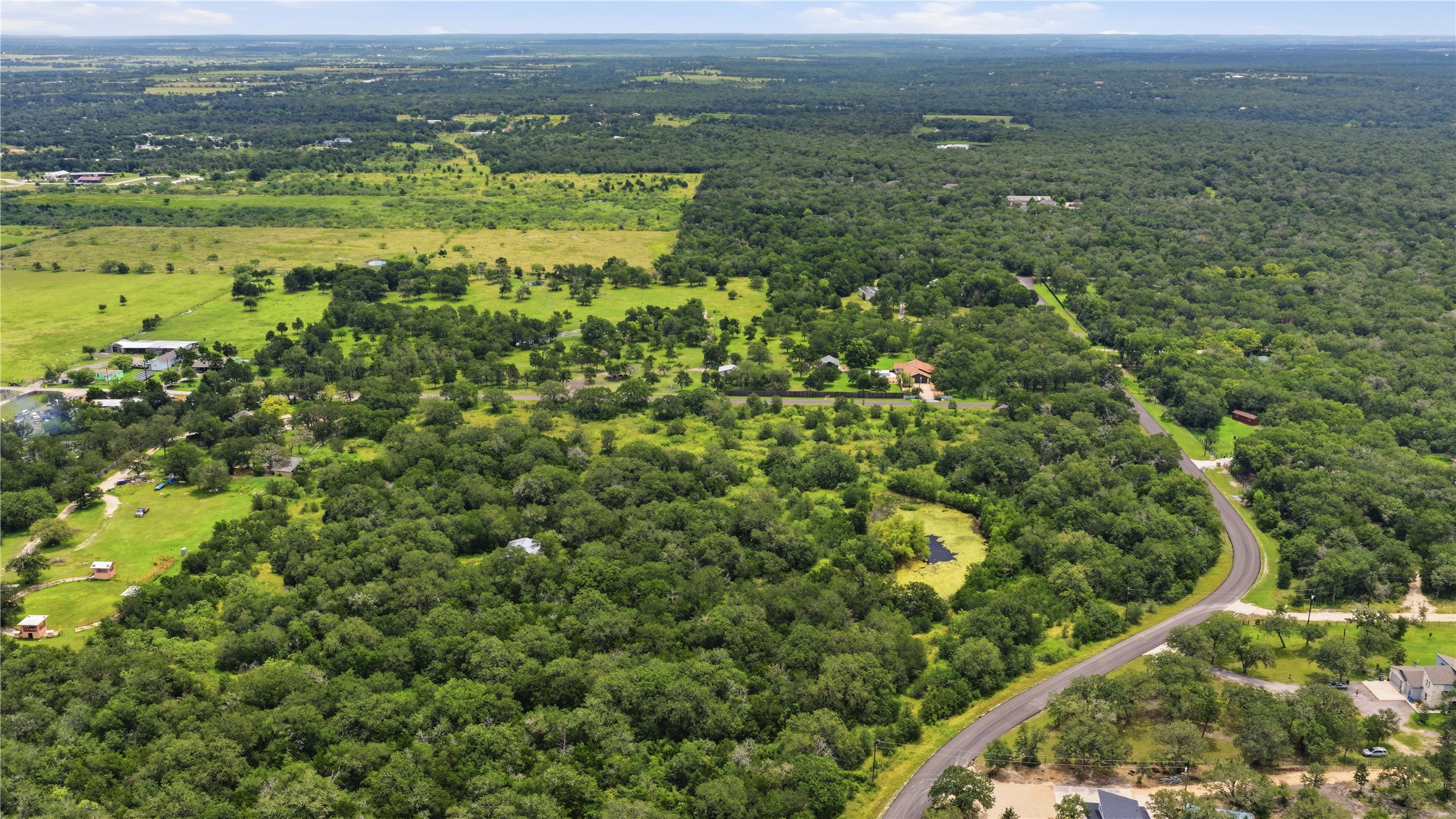 10312 Parsons Road Manor, TX 78653 - Photo 7 of 26 Discover vast green landscapes with an inviting, winding road leading through a serene, tree-dotted estate.