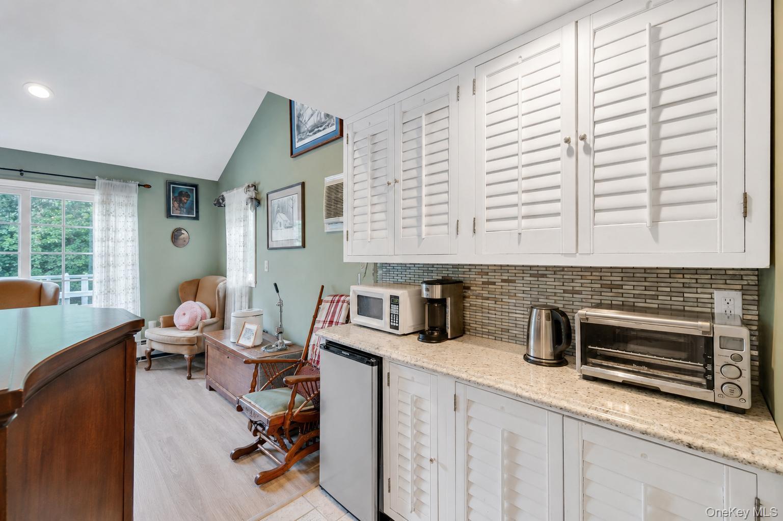 19 Joan Road Bay Shore, NY 11706 - Photo 34 of 50 Galley area featuring white shaker-style cabinetry with louvered doors, a mosaic tile backsplash, and a granite-finish countertop