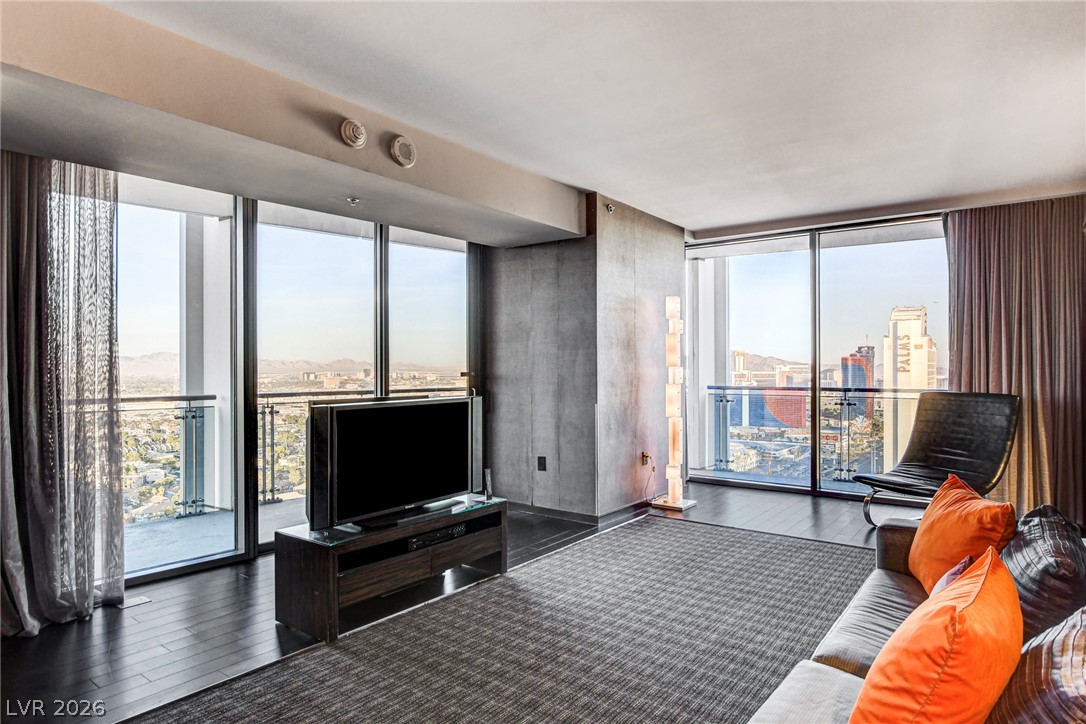 4381 West Flamingo Road, Unit 3002 Las Vegas, NV 89103 - Photo 46 of 59 Towering floor-to-ceiling windows frame panoramic city skyline views across rich hardwood flooring.