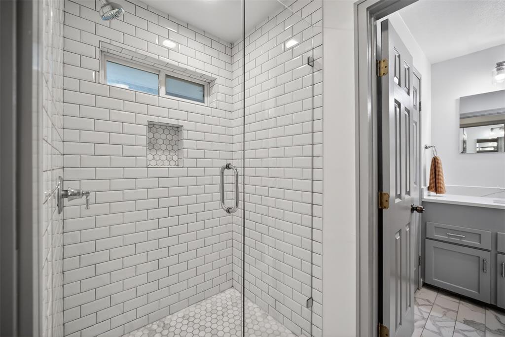9660 Timberleaf Drive Dallas, TX 75243 - Photo 32 of 40 Walk-in shower featuring white subway tile, a chrome showerhead, and a glass enclosure with a rounded handle
