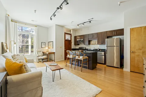 a living room with stainless steel appliances furniture a kitchen view and a window