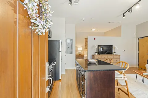 a kitchen with stainless steel appliances granite countertop a refrigerator a stove a sink a dining table and chairs with wooden floor