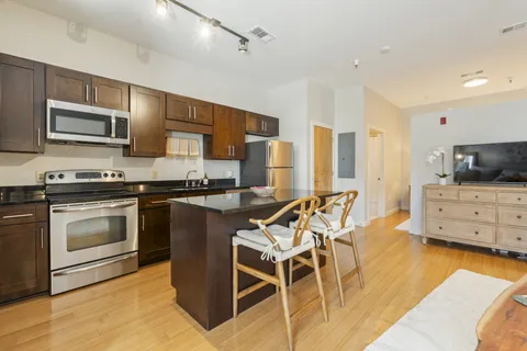 a kitchen with stainless steel appliances kitchen island granite countertop a stove top oven a sink a dining table and chairs with wooden floor