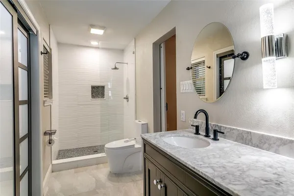 a bathroom with a granite countertop sink a toilet a mirror and shower