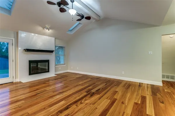 a view of an empty room with wooden floor fireplace and a window