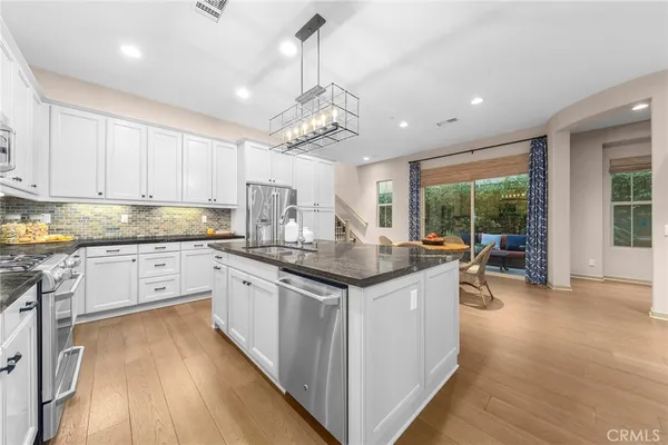 a open kitchen with granite countertop a stove top oven a sink a dining table and chairs with wooden floor