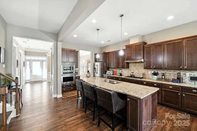 a kitchen with a stove a refrigerator a sink a dining table and chairs with wooden floor