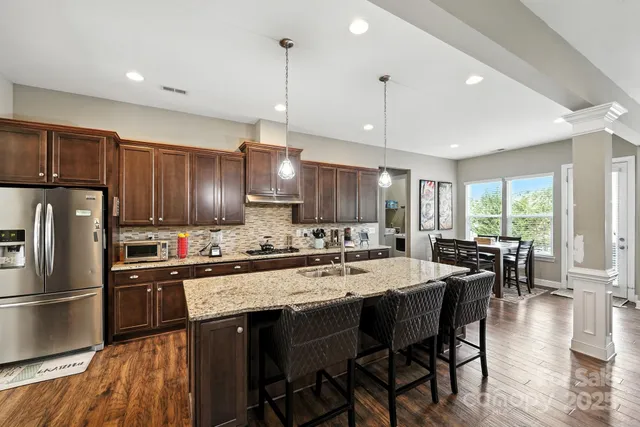 a kitchen with stainless steel appliances granite countertop a stove a refrigerator a sink a dining table and chairs with wooden floor