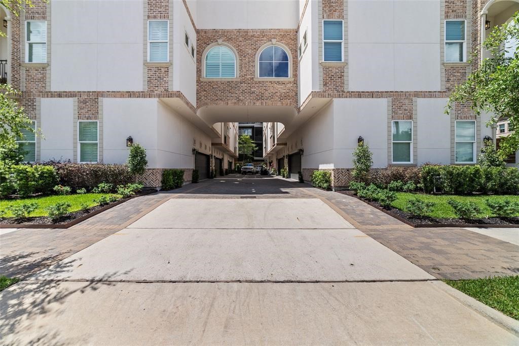710 Delano Street, Unit A Houston, TX 77003 - Photo 1 of 32 The modern townhouse complex with a shared driveway leading to garages. The building features a mix of brick and stucco exterior, with well-maintained landscaping and greenery on both sides. The architecture includes large windows, and there's a central archway providing access to the inner areas.